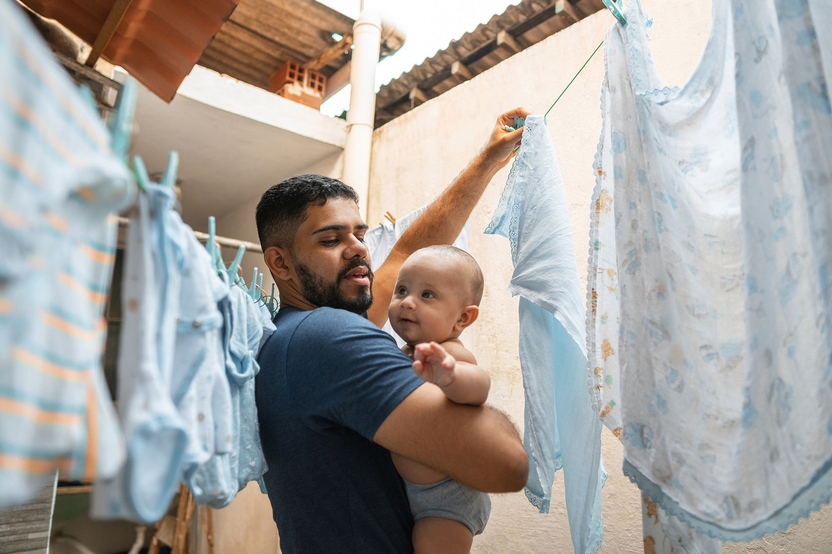 Father line drying clothes while holding a baby