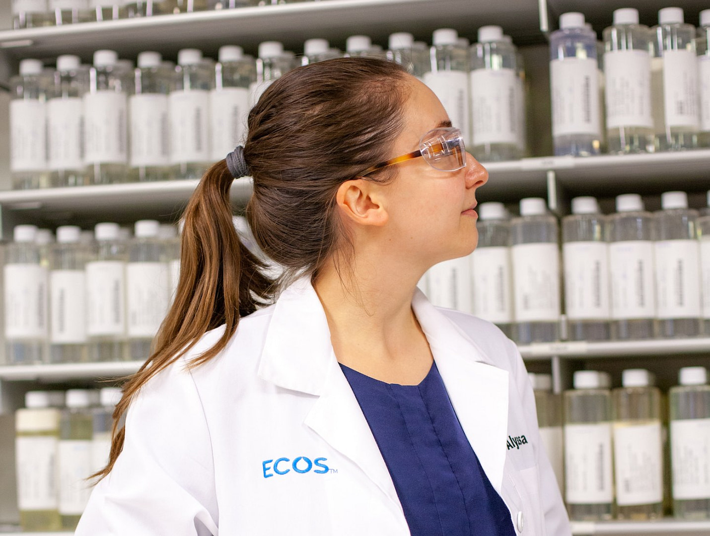 Woman In Lab Coat & Goggles Looking At Bottles